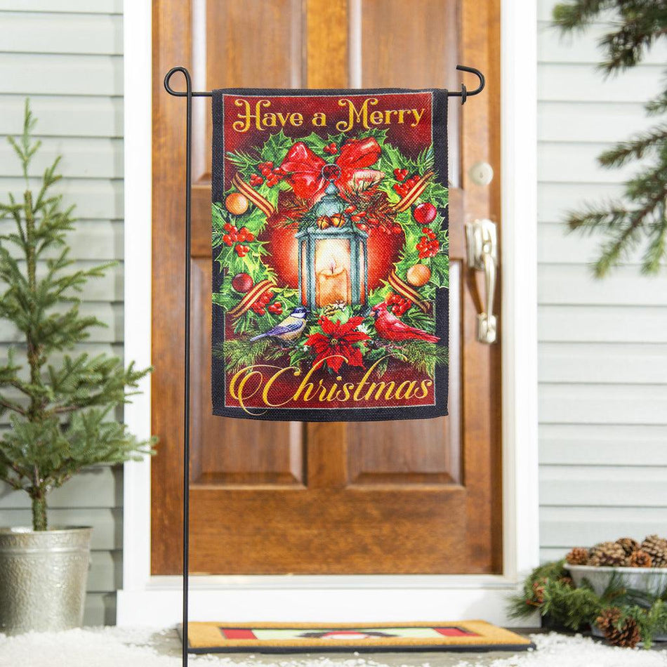 The Have a Merry Christmas Lantern garden flag features a vintage lantern surrounded by a holiday wreath and the words "Have a Merry Christmas".