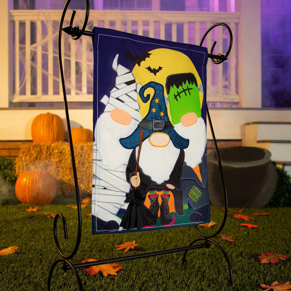 The Trick or Treat Gnomes garden flag features a trio of gnomes dressed in Halloween costumes and ready for trick or treating.