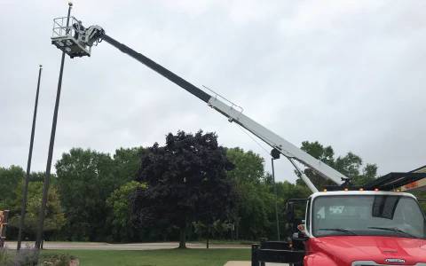 A flagpole being repaired by a repairman on a crane.
