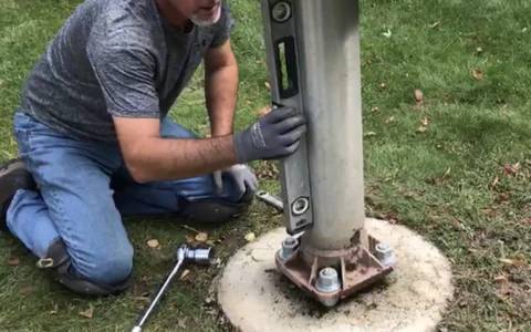 A repairman is replumbing a flagpole and measuring the degree of its lean.
