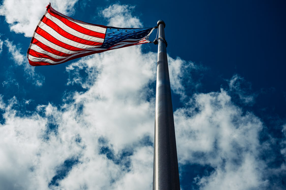An American flag flying high on a flagpole with blue sky and fluffy clouds above it.