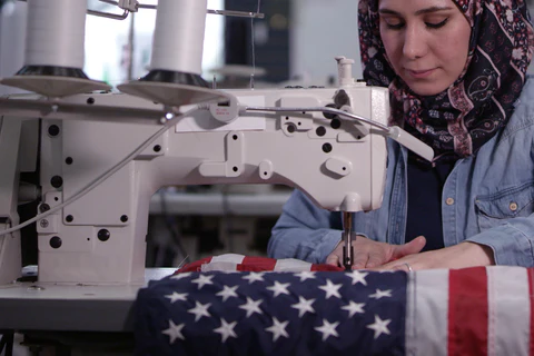 A woman repairs a U.S. flag on a sewing machine