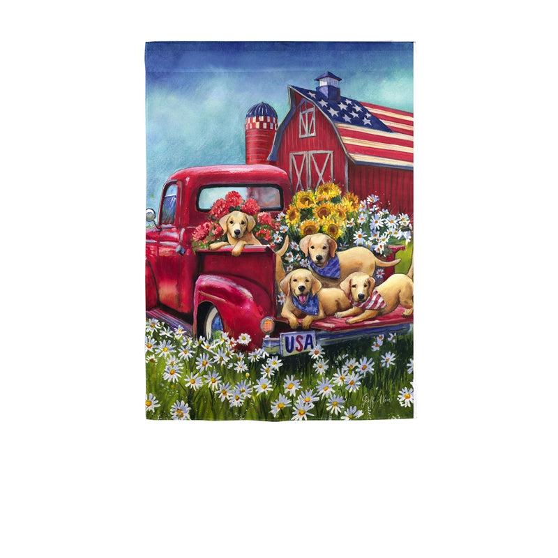 The Americana Dogs garden flag features a group of dogs resting in the back of a red pick-up truck and an American flag on a red barn in the background. 