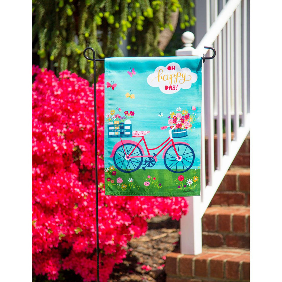 The Bike Ride Blooms garden flag features a pink bicycle with baskets full of flowers and the words" Oh Happy Day".