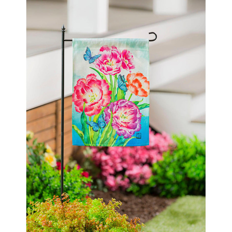 The Blooming Tulips garden flag features blue butterflies among vividly colored tulips in full bloom.