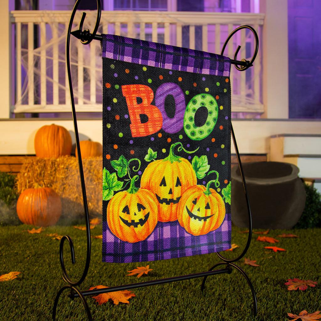 The Boo Jack-O-Lanterns garden flag features a trio of smiling jack-o-lanterns over a purple and black checked and dotted background, and the word "BOO". 