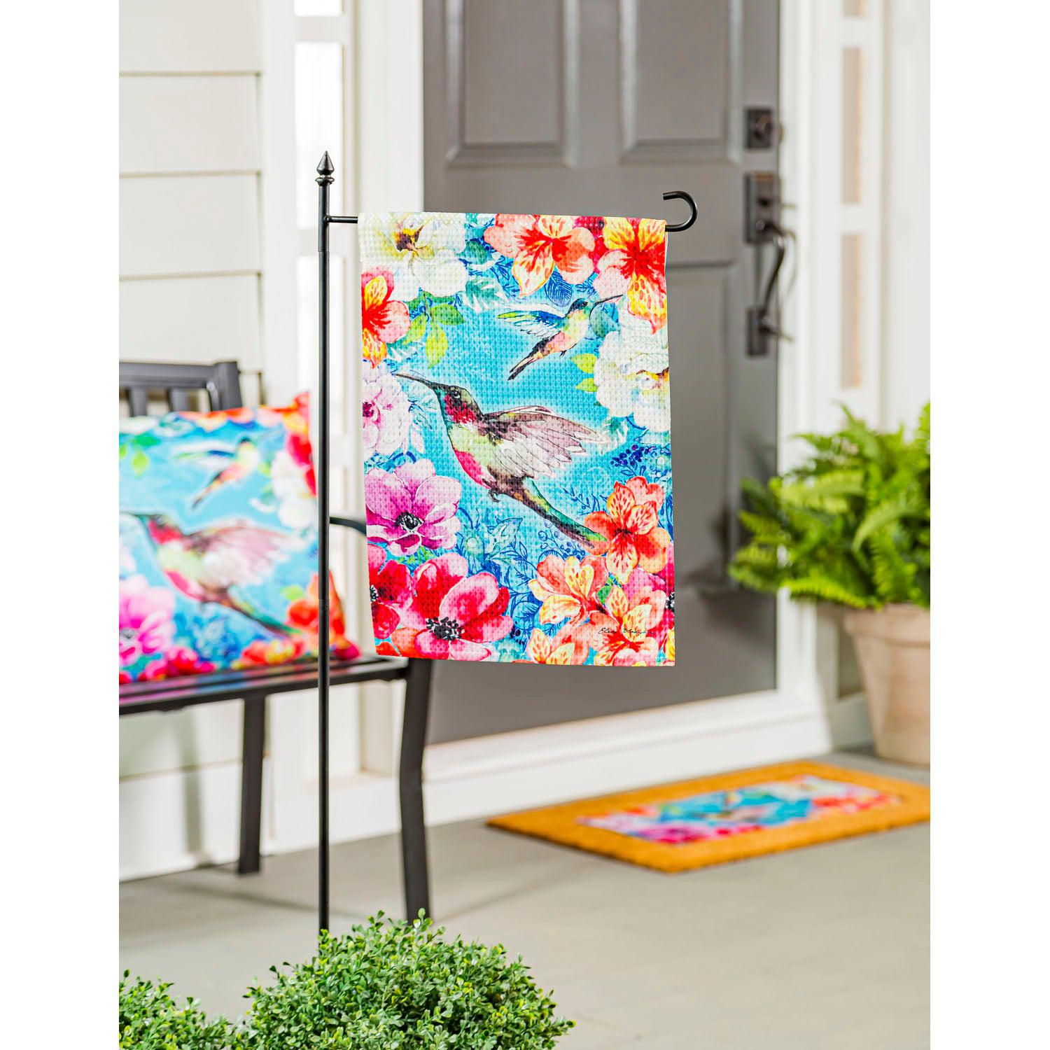 The Bright Flowers and Hummingbirds garden flag features a pair of hummingbirds flying among a multitude of brightly colored flowers. 