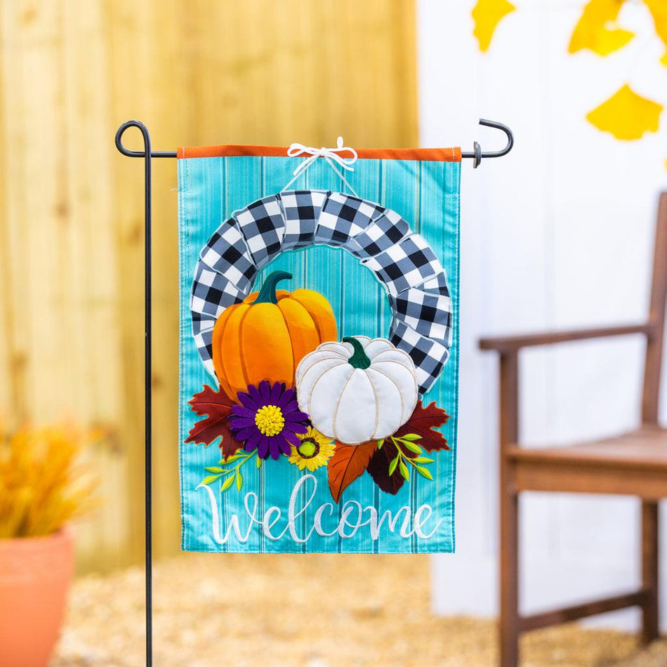 Our Buffalo Check Fall Wreath garden flag features a black and white checked wreath decorated with pumpkin and flowers and the word "Welcome". 
