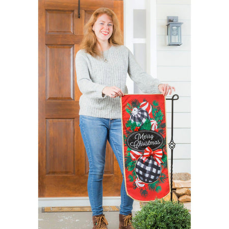 This extra-long garden flag features checked ornaments with candy and bows hanging on pine boughs and the words "Merry Christmas". 
