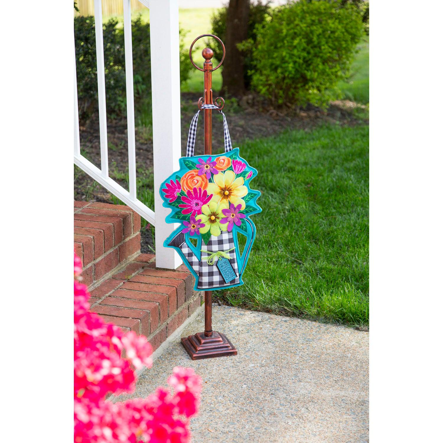 The Buffalo Check Watering Can door décor features a black checked watering can holding a bouquet of flowers and a tag with the words "Welcome Friends". 
