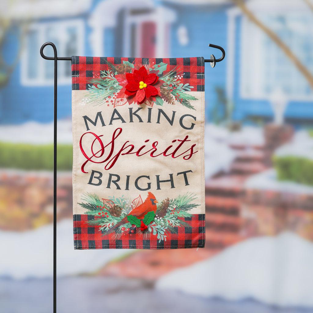 The Christmas Joy garden flag features a poinsettia, a cardinal, a black and red checked border, and the words "Making Spirits Bright".