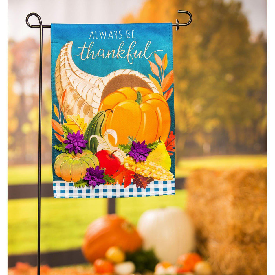 The Cornucopia With Checks garden flag features a cornucopia with fall fruits and vegetables and the words "Always Be Thankful". 