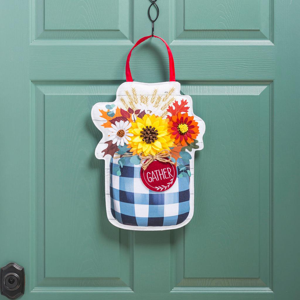 The Fall Check Mason Jar door décor features an array of fall flowers in a black checked mason jar with a tag that says "Gather". 