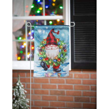 The Gnome With a Christmas Wreath garden flag features a smiling gnome sporting a pine wreath decorated in Christmas lights. 