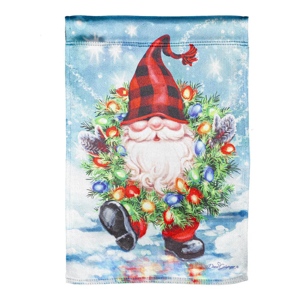 The Gnome With a Christmas Wreath garden flag features a smiling gnome sporting a pine wreath decorated in Christmas lights. 