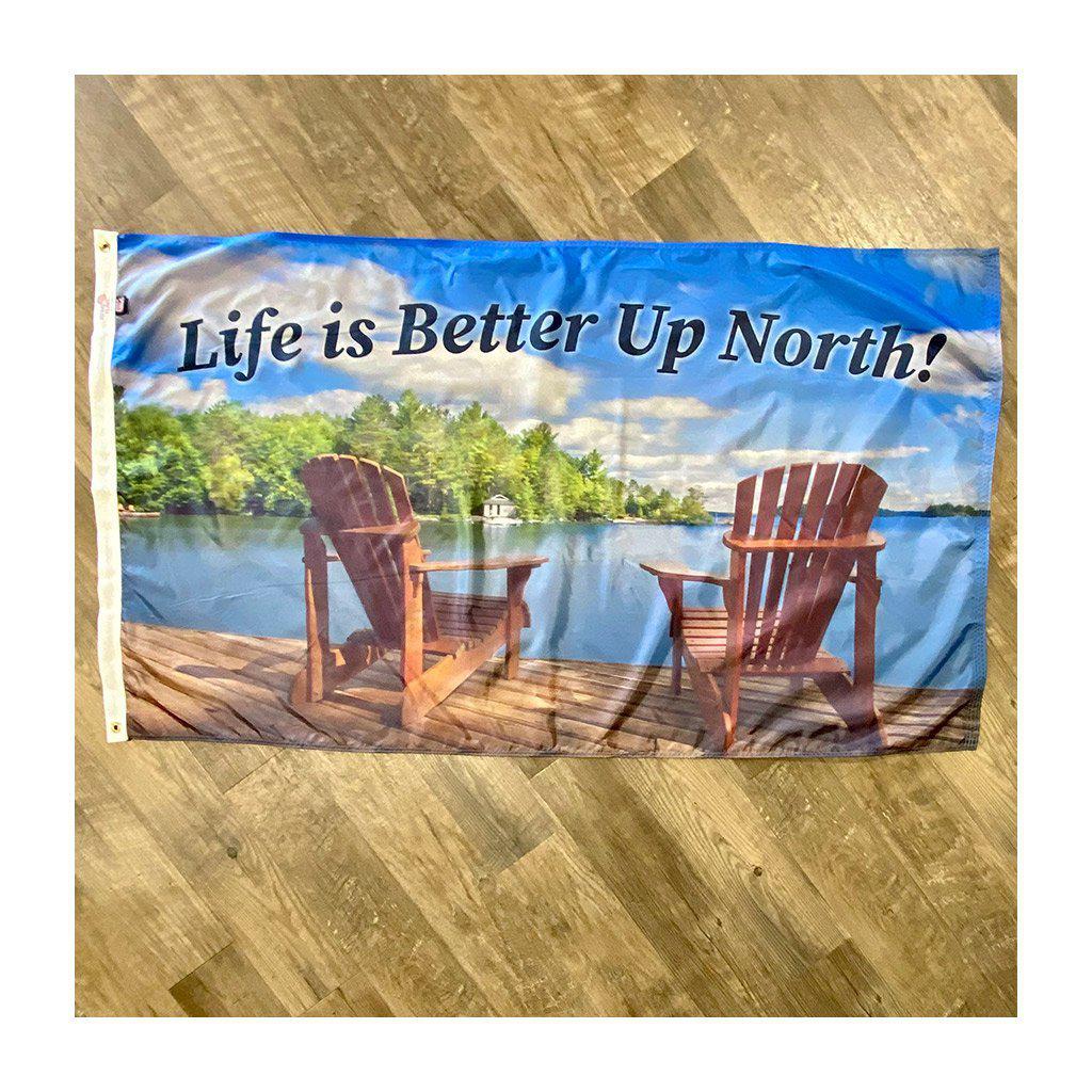 This 3' x 5' flag features adirondack chairs on a pier overlooking the water and the words "Life is Better Up North" across the top of the flag.