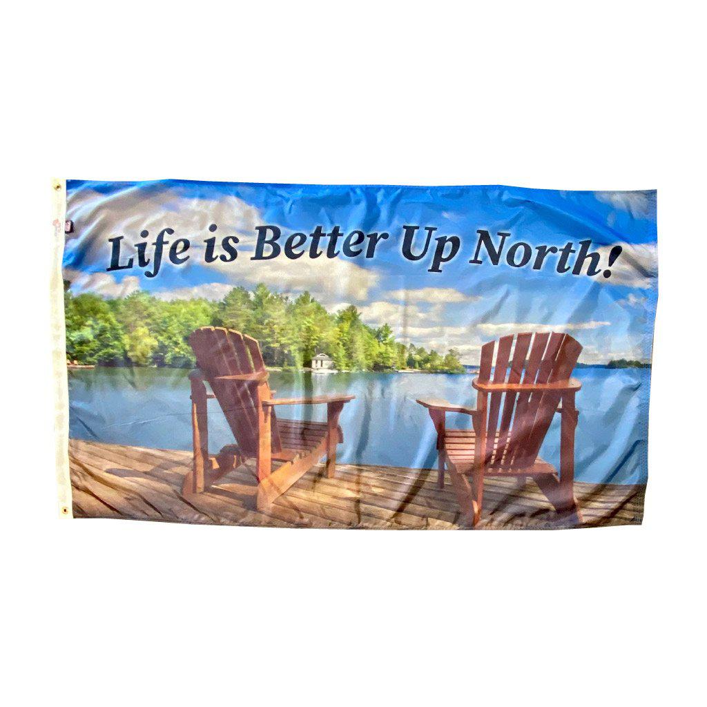 This 3' x 5' flag features adirondack chairs on a pier overlooking the water and the words "Life is Better Up North" across the top of the flag.