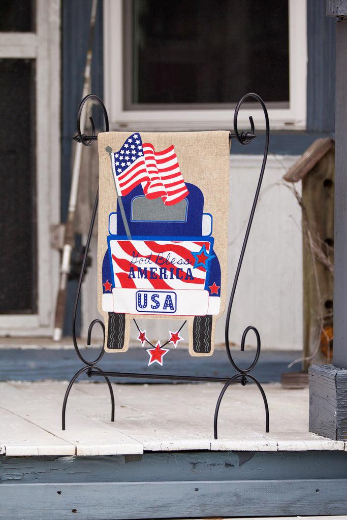 The Patriotic Pick-Up Truck garden flag features a blue truck flying a U.S. flag with a U.S.A. license plate and the words "God Bless America" across the striped tailgate.