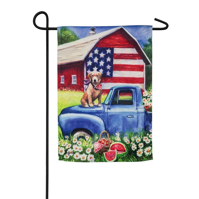The Patriotic Pup garden flag features a dog sitting on the hood of a blue pick-up truck and an American flag on a red barn. 