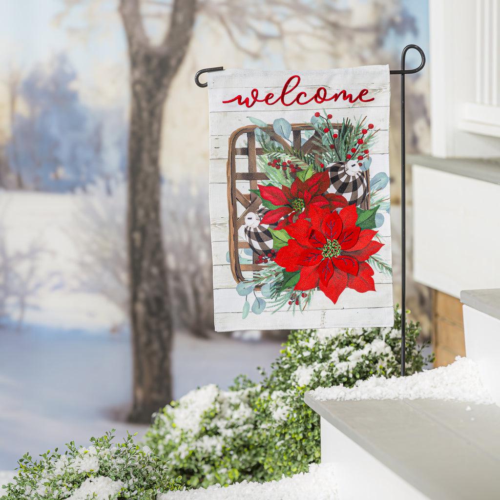 The Poinsettia Tobacco Basket garden flag features red poinsettias and buffalo checked ornaments on a tobacco basket with the word "Welcome" across the top.