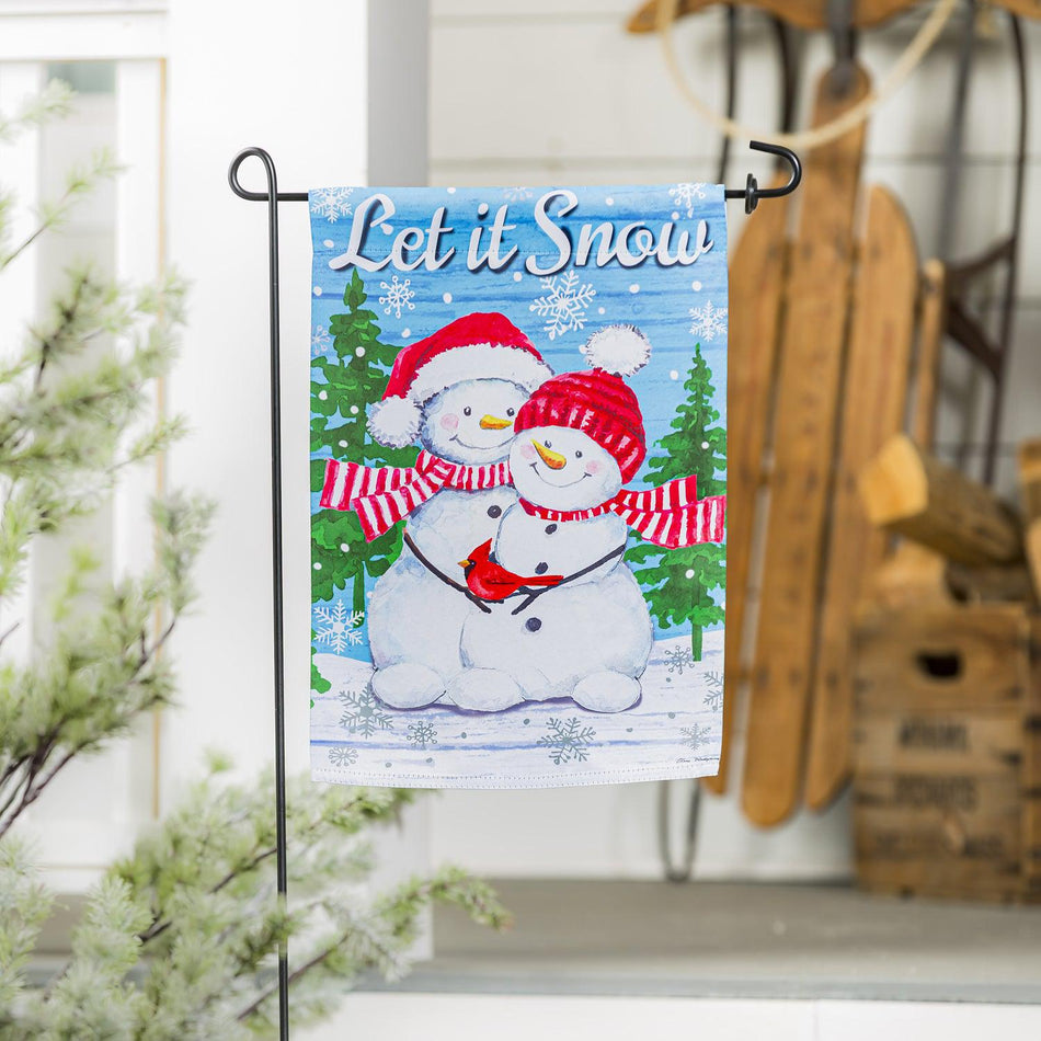 The Snowman Family garden flag features a smiling snow couple with red hats and scarves holding a cardinal along with the words "Let it Snow".