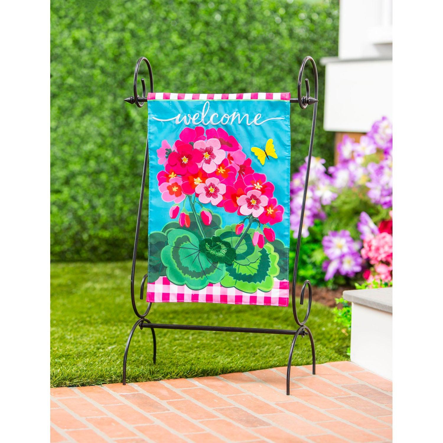 The Spring Geraniums garden flag features vivid pink geraniums with hot pink checked top and bottom borders and the word "Welcome" across the top.