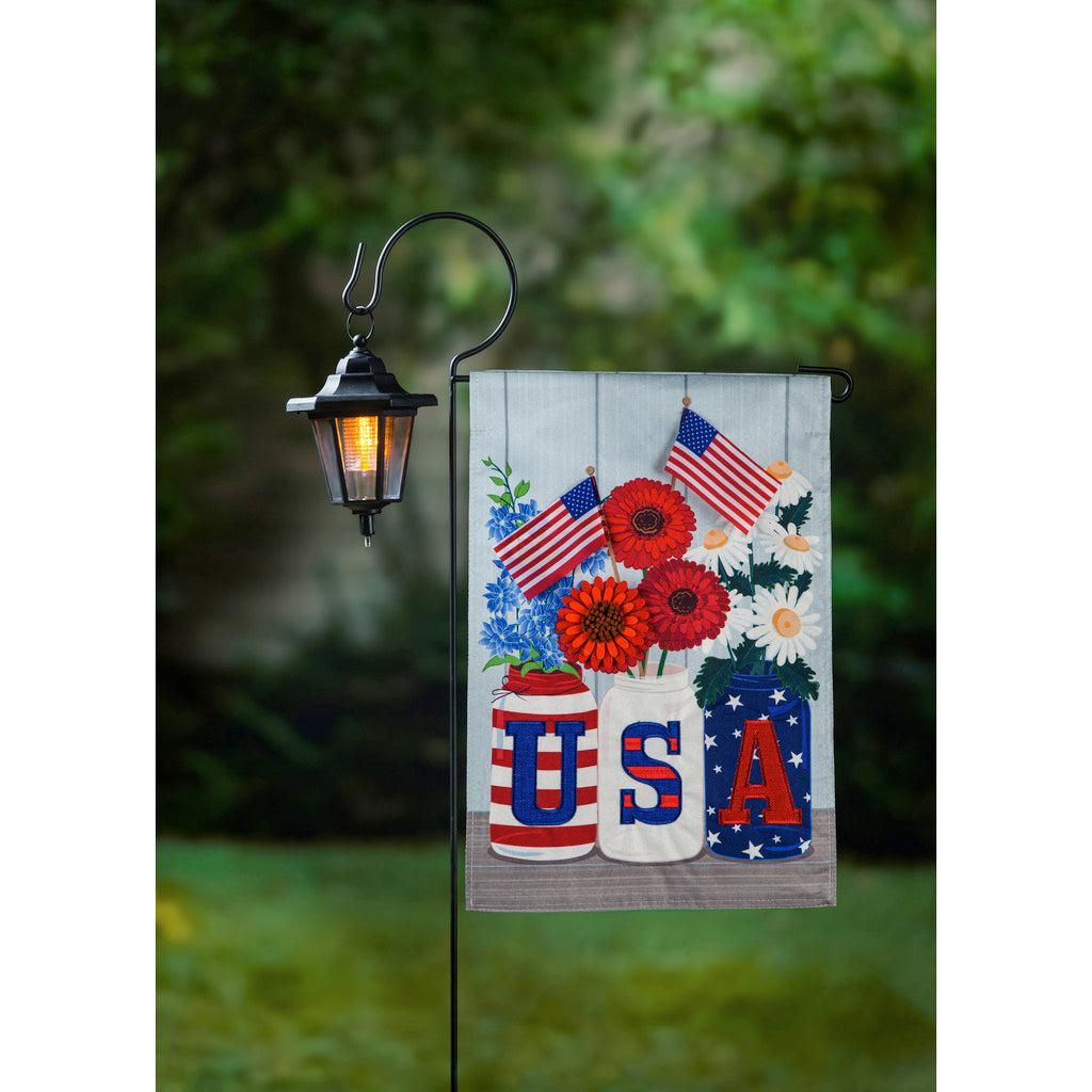 The USA Mason Jar garden flag features three mason jars with the letters USA on the front, holding flags and red, white, and blue flowers.