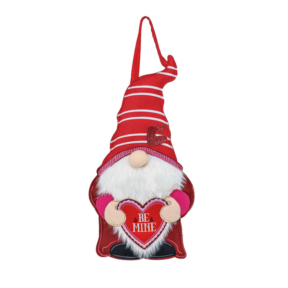 The Valentine Gnome Door Décor features a gnome dressed in red holding a heart with the words "Be Mine". 