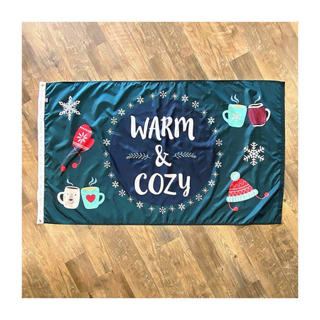 Our 3' x 5' Warm & Cozy Winter flag features snowflakes, a hat, mittens, and warm drinks along with the words "Warm & Cozy" on a navy and dark teal background.