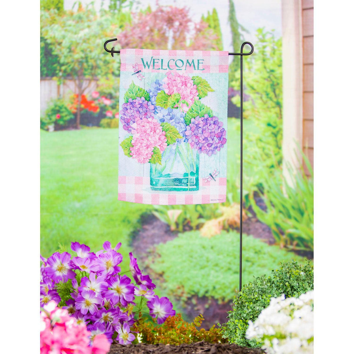The Welcome Hydrangeas garden flag features pink, blue, and lavender hydrangeas in a vase, a pink checked top and bottom border, and the word "Welcome "across the top. 