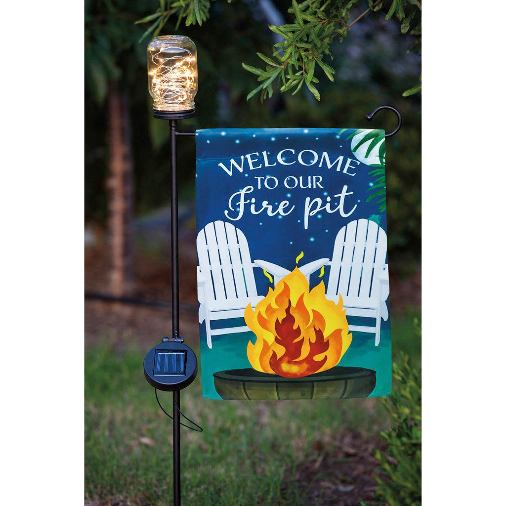 The Welcome to Our Firepit garden flag features lawn chairs, a roaring fire, and the words "Welcome to Our Firepit" across the top. 