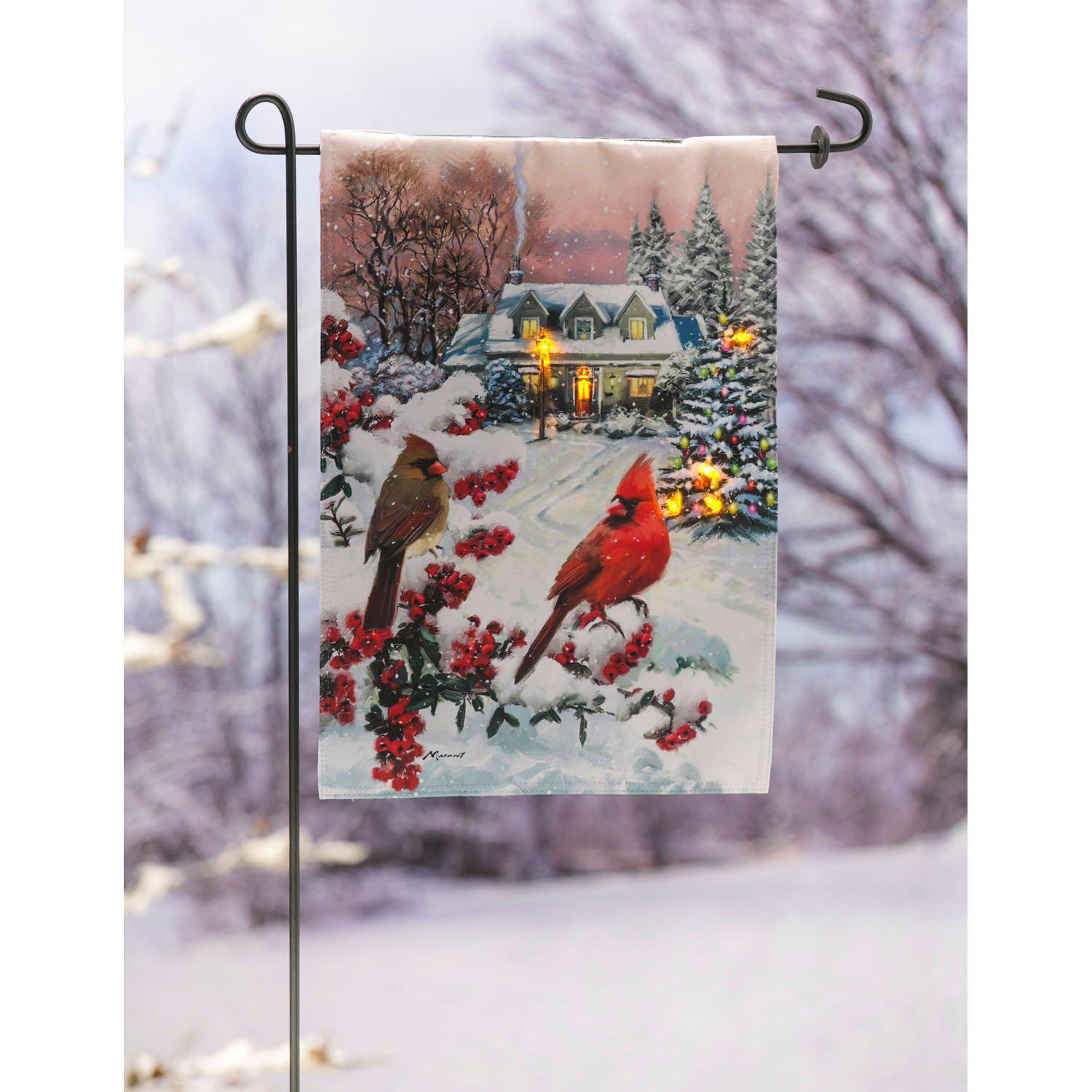 The Winter Perch Solar LED garden flag features a pair of cardinals sitting on snow covered branches with a cozy home in the background. 